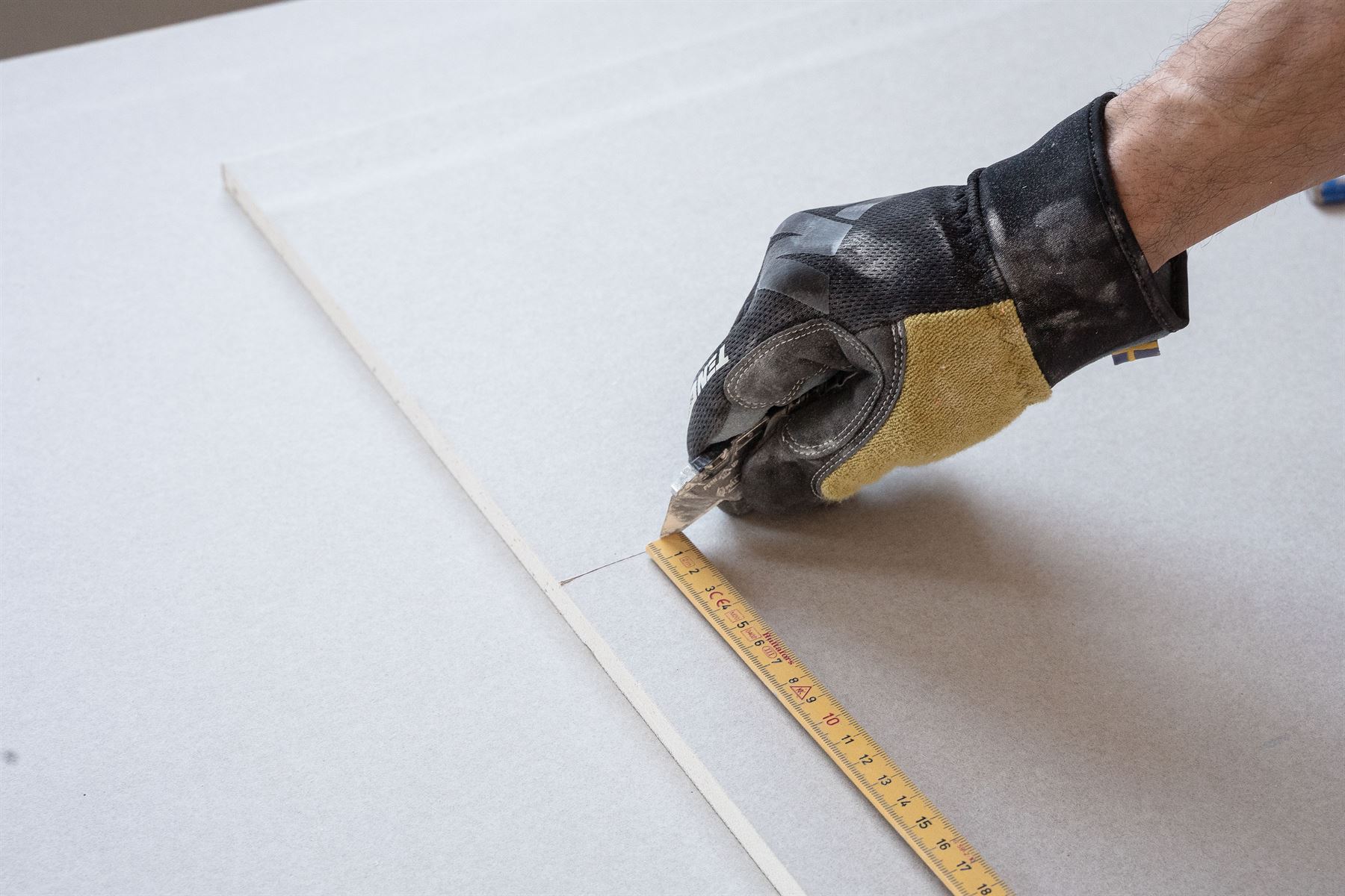 Hand im Arbeitshandschuh legt einen Meterstab an eine Platte an