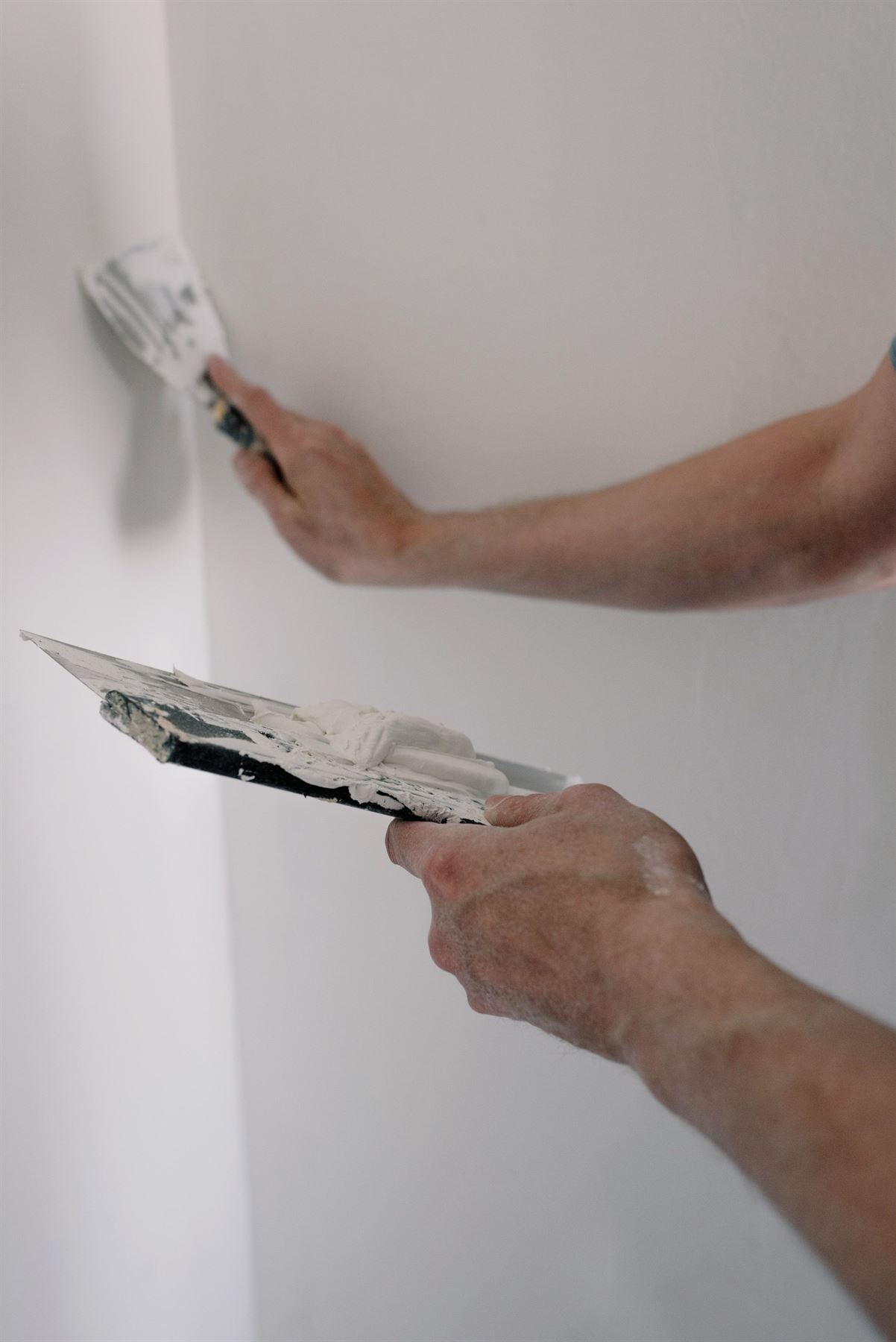 Hände glätten eine helle Wand mit dem Spachtel